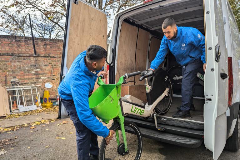 Two uniformed RBKC officers unloading a seized rental e-bike from a white van